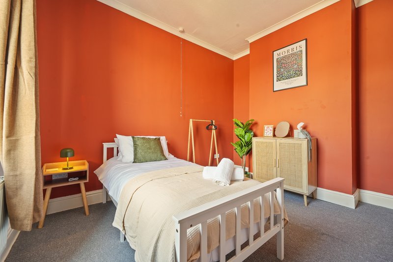 Bedroom with single bed, orange walls, wooden furniture, and potted plant