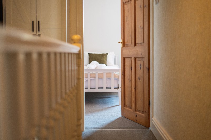 Hallway with wooden door leading to bedroom with white bed and olive cushion