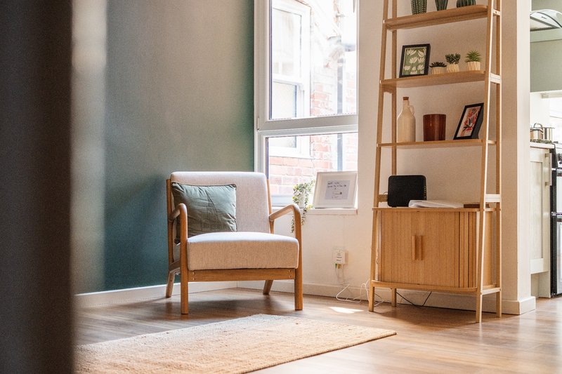 Bright living room with upholstered armchair, wooden shelving unit, and large windows