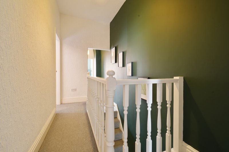 Hallway with white staircase railing, green accent wall, and cream-colored walls