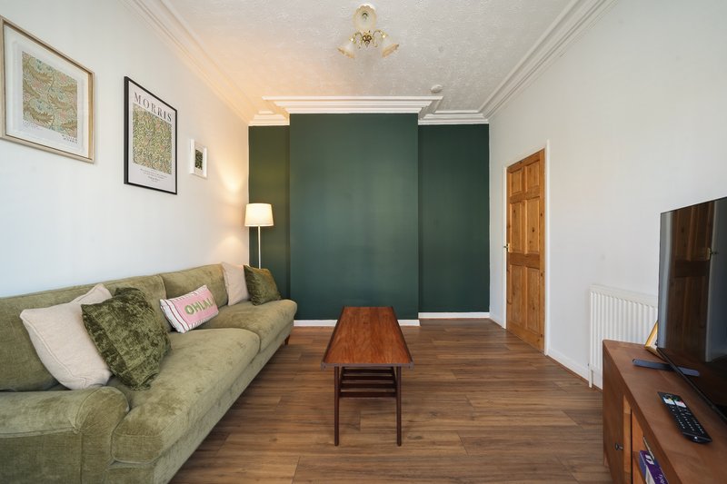 Living room with green sofa, wooden coffee table, dark green accent wall, and framed artwork
