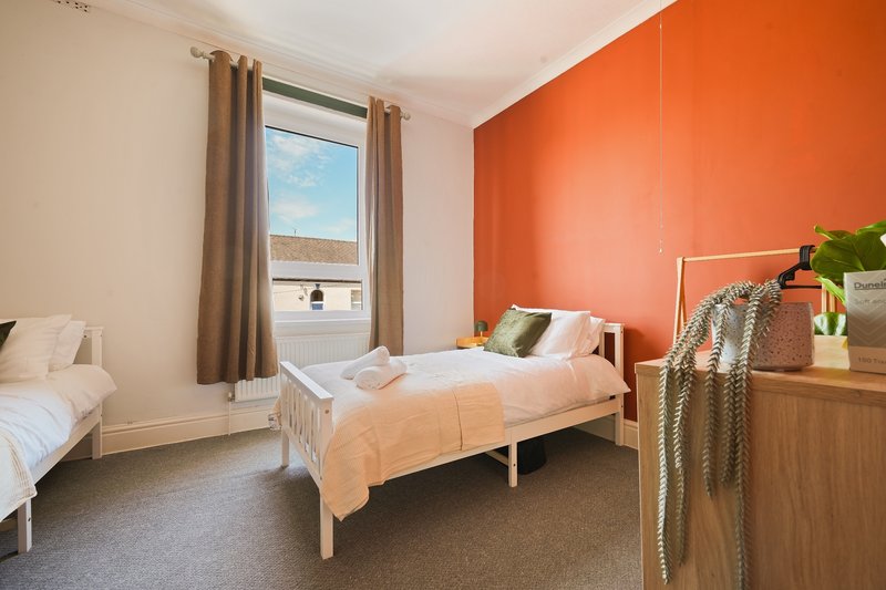 Bright bedroom with two single beds, orange accent wall, wooden furniture and large window