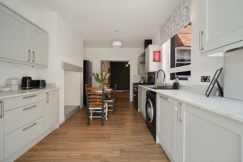 Modern galley kitchen with white cabinetry, wooden flooring, integrated appliances and dining area