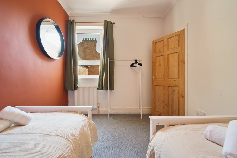Bright twin bedroom with two single beds, round mirror, window with curtains, wooden door