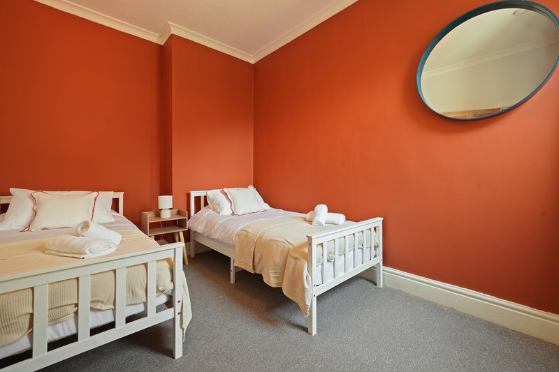 Bright orange bedroom with two white single beds, grey carpet, and round mirror