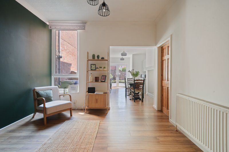 Modern hallway with wooden flooring, green accent wall, armchair, and view into adjoining rooms