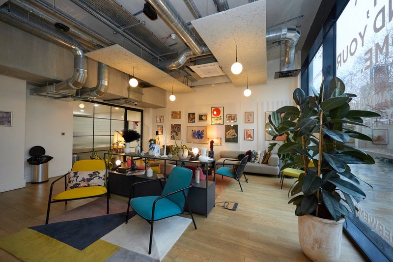 Modern open-plan living space with colorful mid-century furniture, exposed ceiling, and wall art gallery
