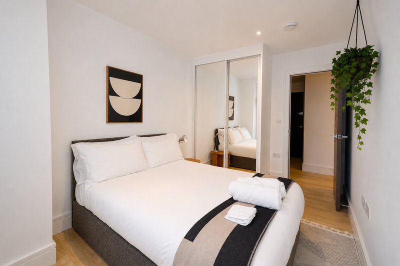 Modern bedroom with double bed, mirrored wardrobe, wooden floor and hanging plant