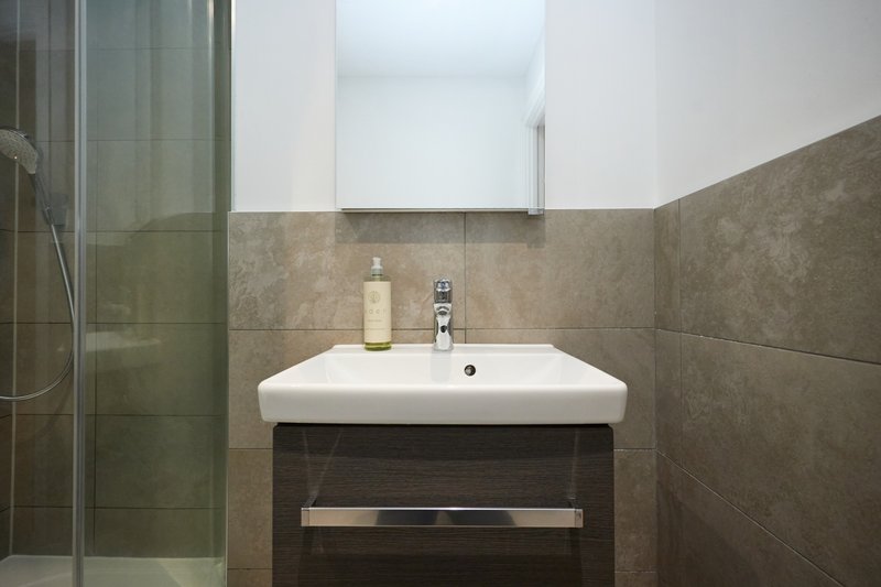 Modern bathroom with white sink, dark vanity unit, tiled walls and glass shower enclosure