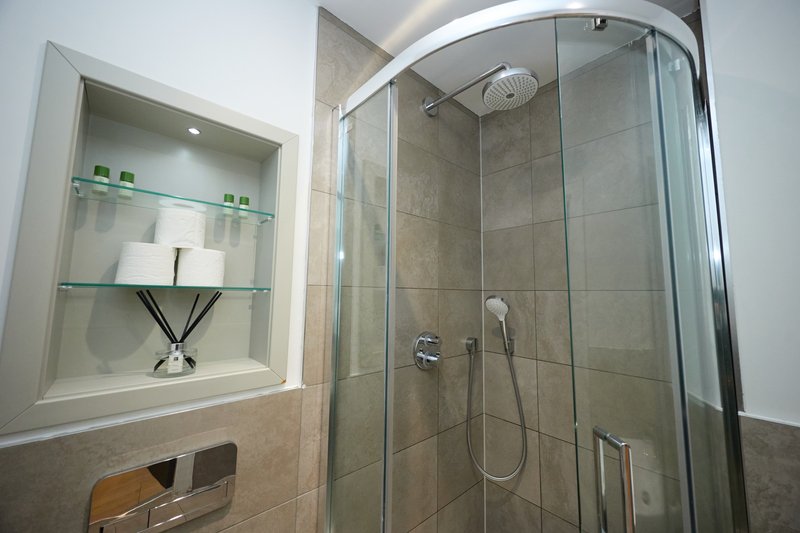 Modern bathroom with curved glass shower enclosure, tiled walls, and recessed shelving