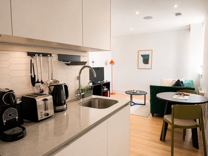 Modern kitchen with white cabinetry, stainless steel sink, and dining area with green chairs
