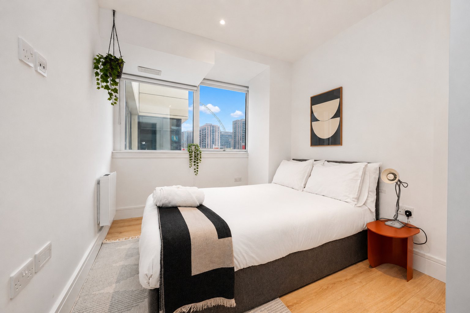 Modern bedroom with double bed, wooden floor, hanging plant and city skyline view