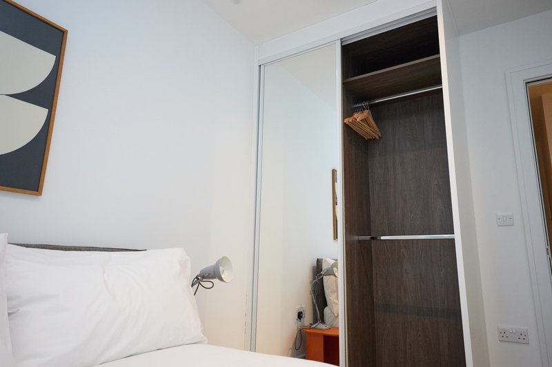 Compact bedroom with white bed, built-in wardrobe, and framed wall art
