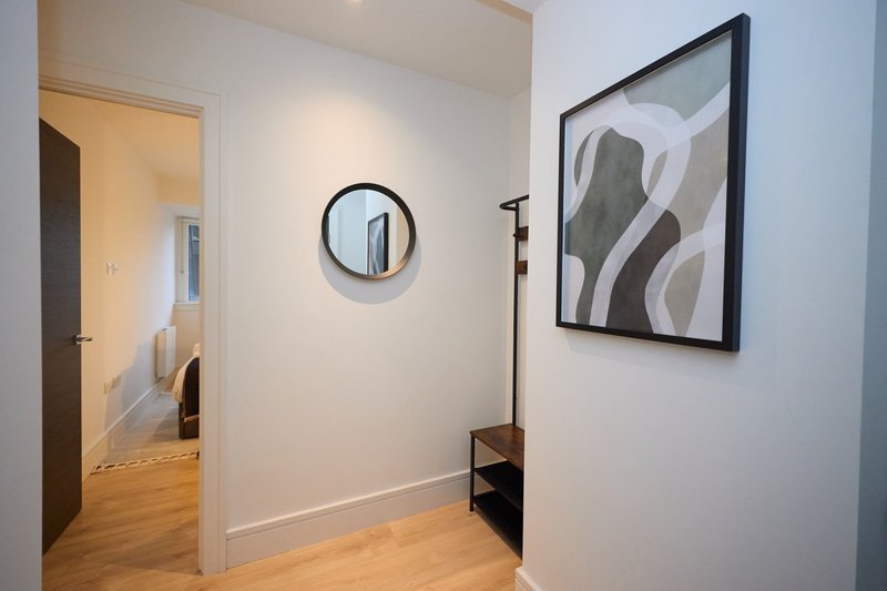 Modern hallway with wooden flooring, circular mirror, abstract framed artwork, and open doorway to adjacent room