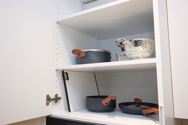 Open kitchen cabinet shelves displaying cookware and storage baskets with handles