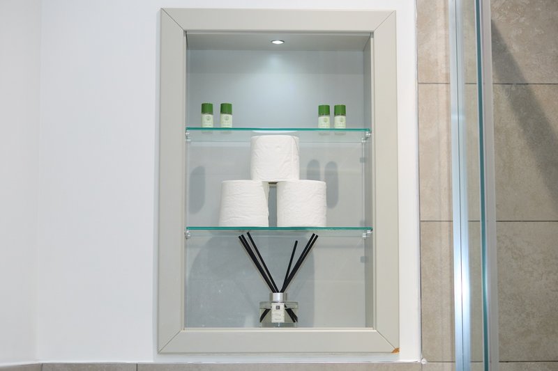 Bathroom wall niche with glass shelves displaying toiletries, rolled towels and reed diffuser