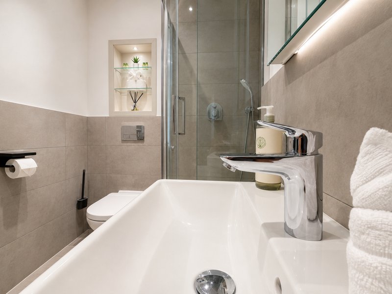 Modern bathroom with white bath, walk-in shower, beige tile walls and heated towel rail
