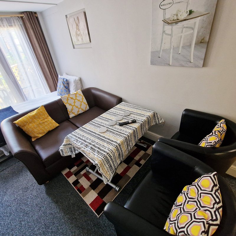Living room with brown leather sofa, black armchairs, patterned rug and yellow accent cushions