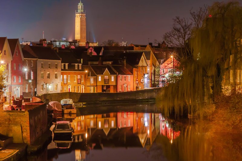 Historic riverside town at dusk with illuminated buildings reflected in calm water