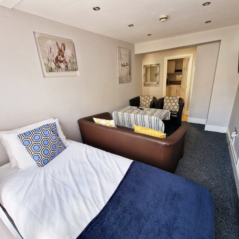 Bedroom with two single beds, brown sofa, patterned cushions, and en-suite bathroom visible