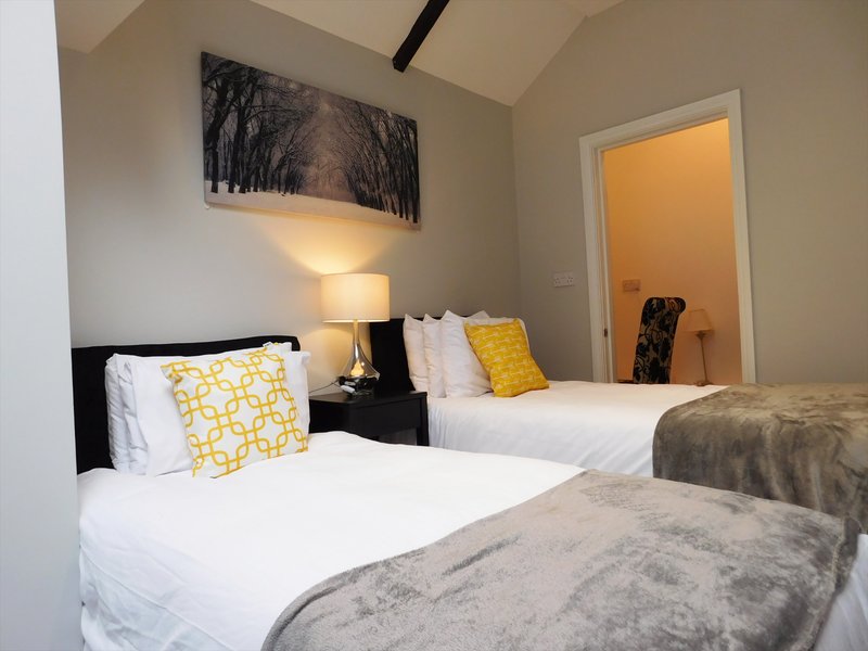 Bedroom with two single beds, white linens, yellow cushions, bedside lamp and wall art