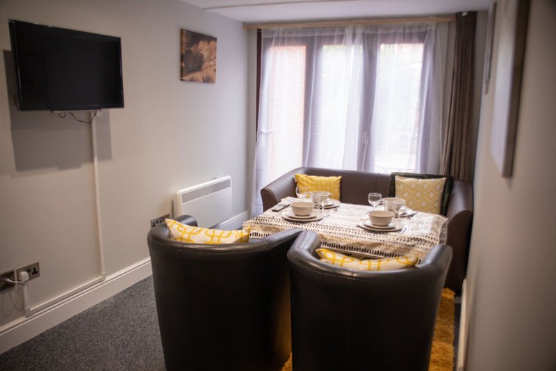 Living room with two black curved sofas, yellow cushions, wall-mounted TV, and large window with curtains