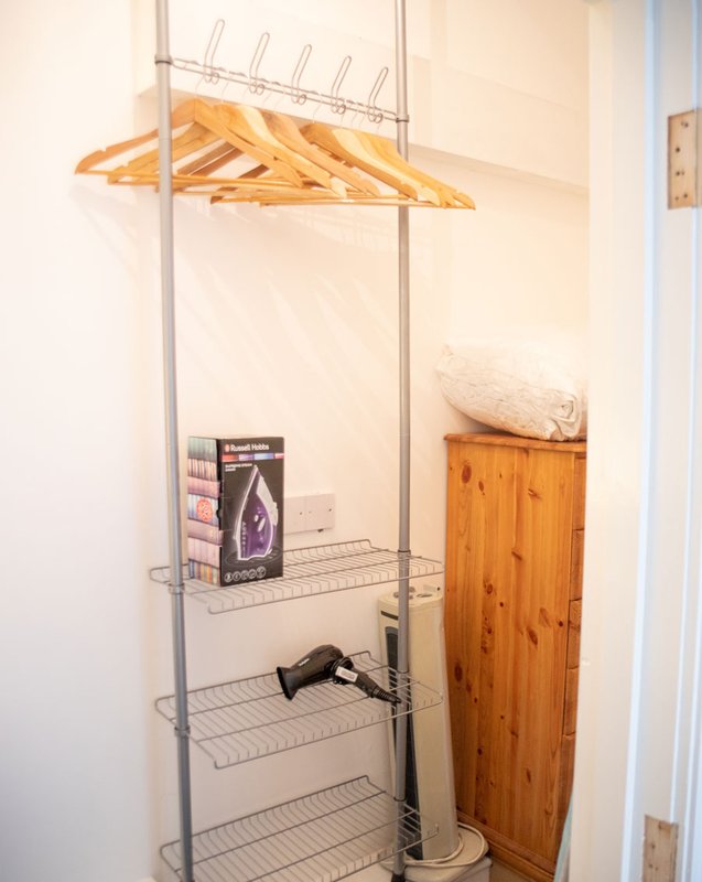 Utility closet with metal shelving unit, wooden hangers, iron, and storage boxes