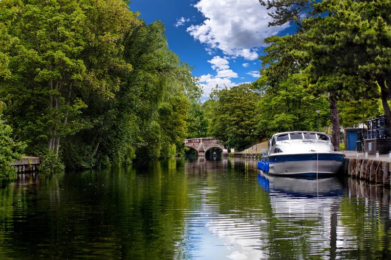 Riverside waterway with moored boat, trees, and stone bridge in background