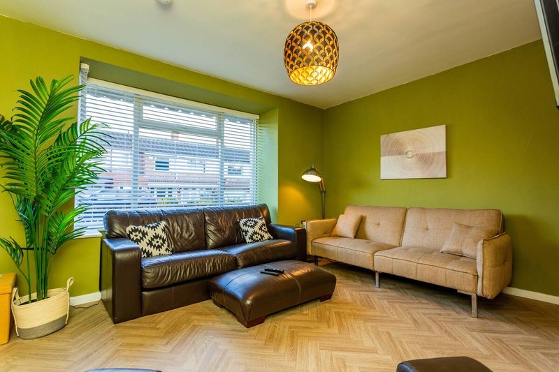 Bright living room with lime green walls, black leather sofa, tan couch, and wooden herringbone flooring