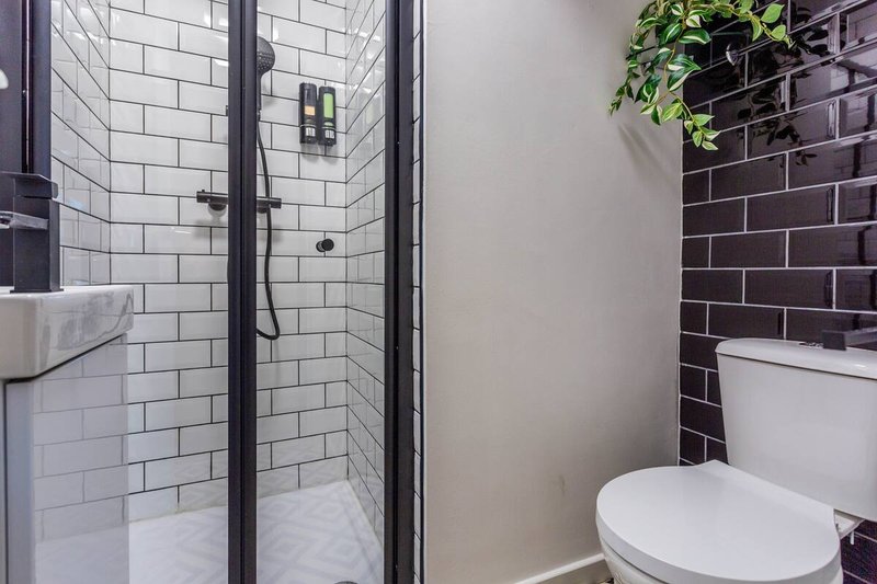 Modern bathroom with walk-in shower, white tile walls, toilet, and dark brick accent wall