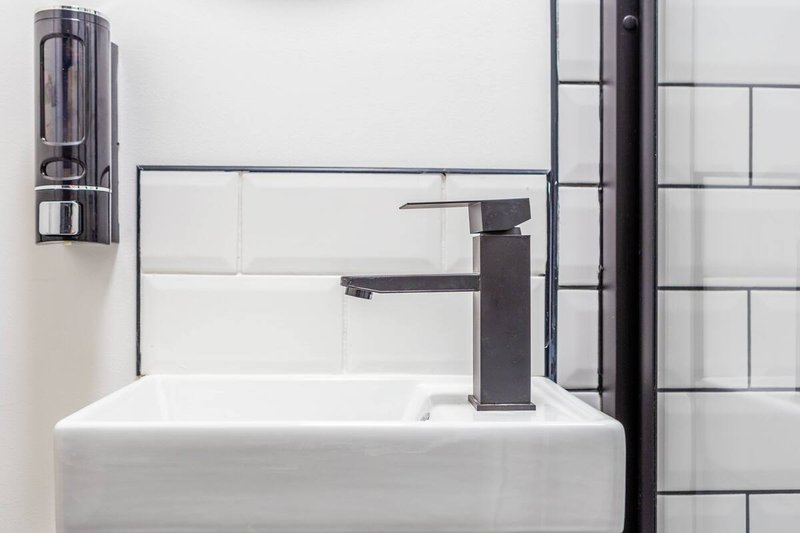 Modern bathroom sink with black tap, white subway tiles, and wall-mounted soap dispenser