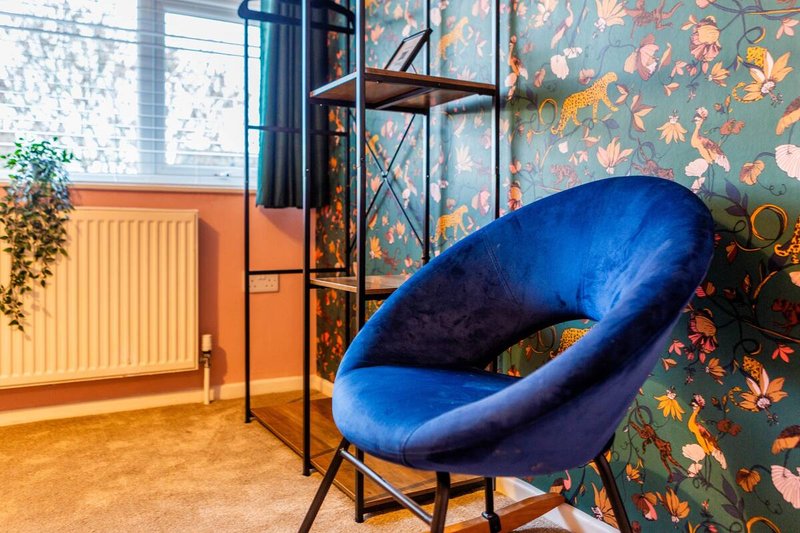 Modern interior with blue curved chair, metal shelving, floral wallpaper and orange radiator