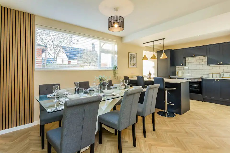 Open-plan kitchen and dining area with dark dining table, grey chairs, and modern black kitchen cabinetry