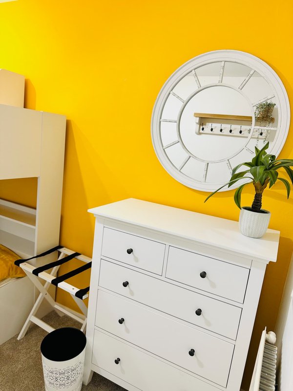 Bright yellow bedroom with white dresser, circular wall clock, potted plant and chair