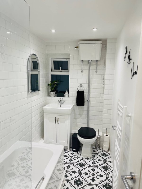 Modern bathroom with white subway tile walls, patterned floor tiles, sink with mirror and black toilet