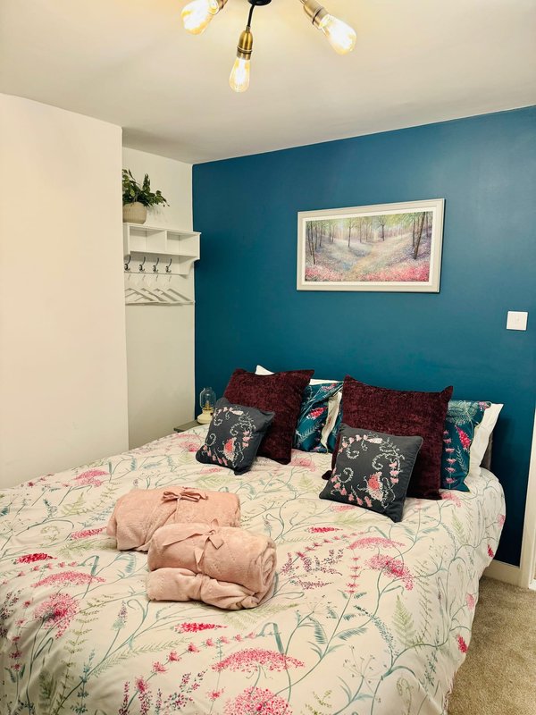 Bedroom with double bed, floral bedding, decorative pillows, teal accent wall, and framed artwork