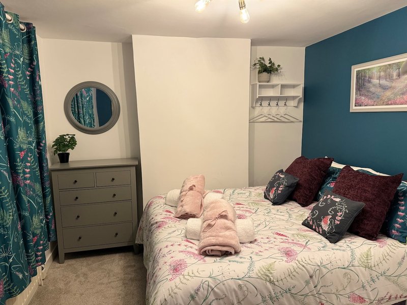 Bedroom with double bed, grey dresser, round mirror, teal accent wall and curtains