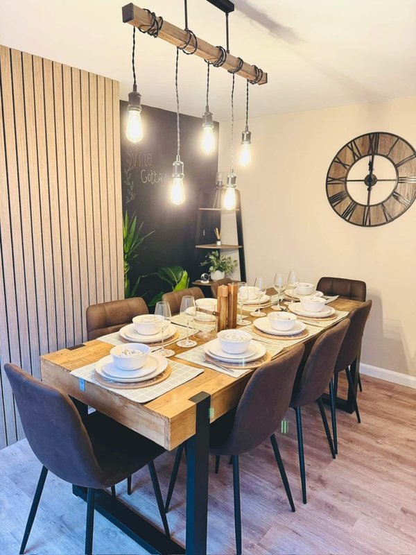 Modern dining room with wooden table, place settings, pendant lighting and wall clock