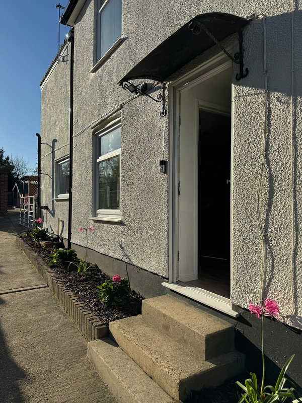 Exterior side view of rendered property with entrance door, black awning, windows and potted flowers