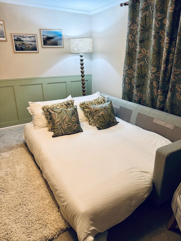 Bedroom with double bed, green headboard, patterned pillows and curtains, wall art