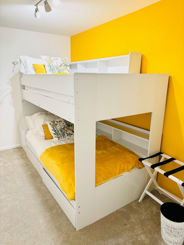 Bright bedroom with white triple bunk bed, yellow bedding, and yellow accent wall