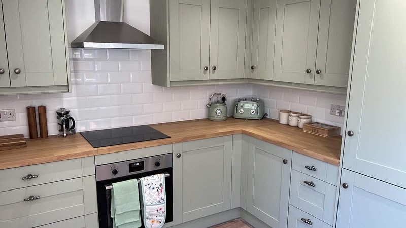Modern kitchen with cream cabinets, wooden countertop, black range cooker and white subway tile splashback