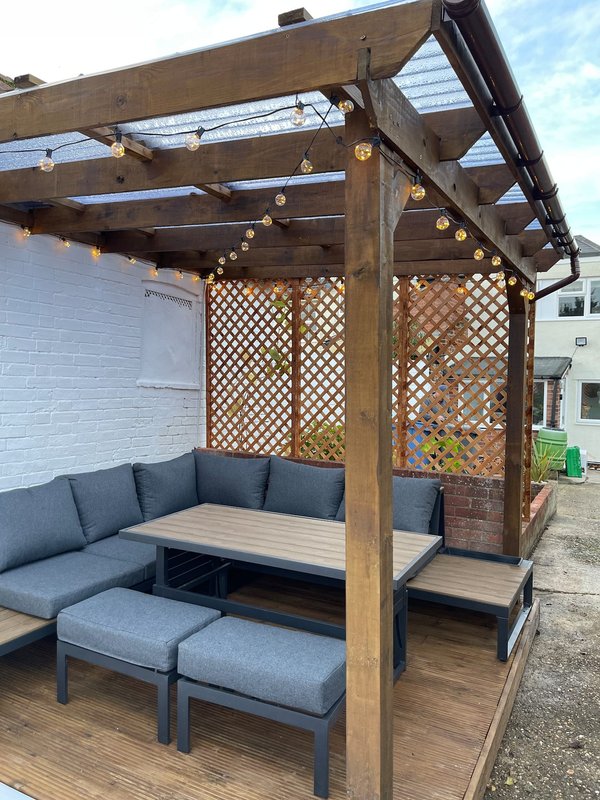 Wooden pergola with lattice panels, built-in seating, and string lights on deck