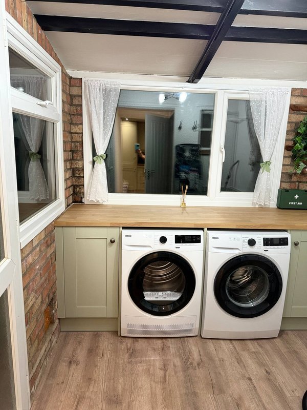 Laundry room with two white washing machines, wooden counter, brick wall and large window