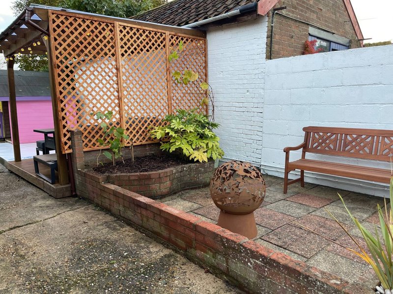 Garden patio area with wooden lattice pergola, planter boxes, decorative terracotta pot and bench seating