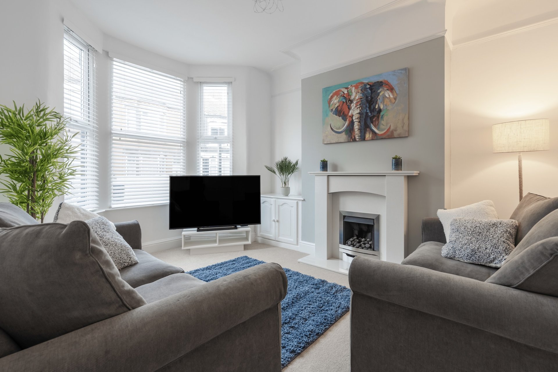 Bright living room with two grey sofas, TV, fireplace, and bay windows