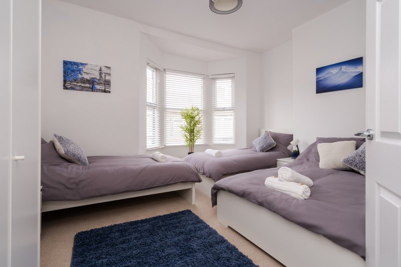 Bright twin bedroom with two beds, purple bedding, blue wall art and bay window