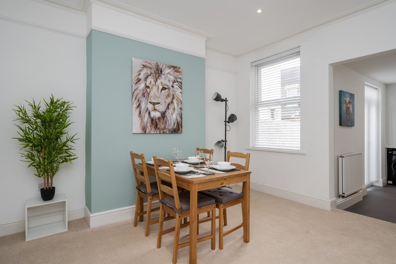 Open-plan dining area with wooden table, chairs, potted plant, and lion artwork on turquoise wall