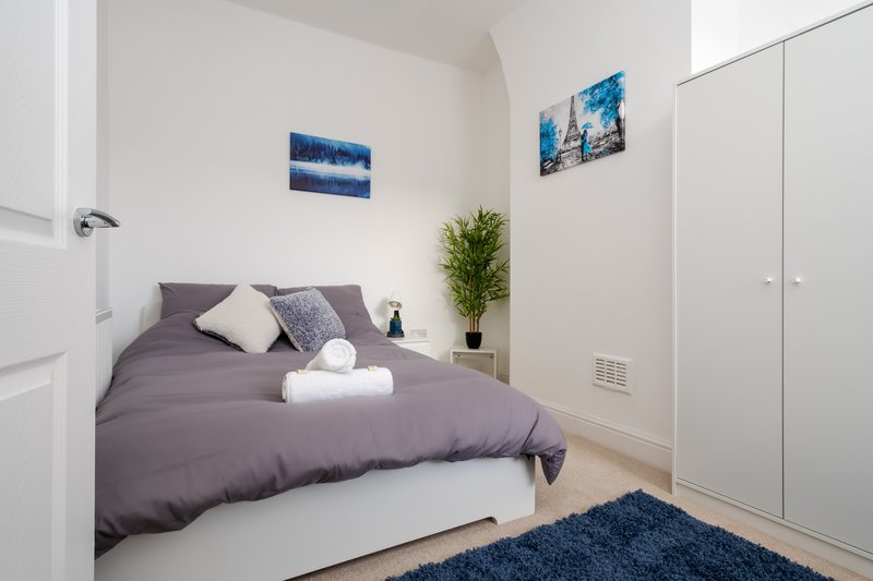 Modern bedroom with double bed, grey bedding, white pillows, blue rug and wall art