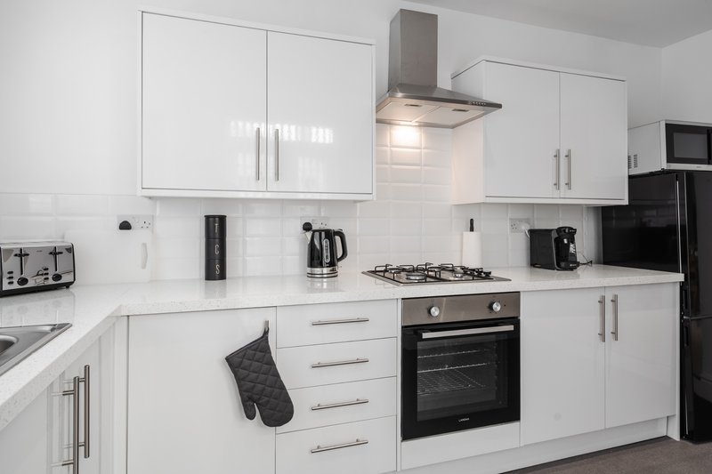 Modern kitchen with white cabinetry, black countertops, integrated appliances and backsplash